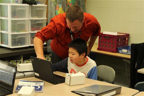 teacher helping boy with computer 