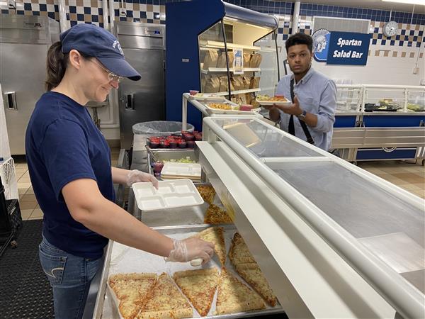 School nutrition employee serves pizza to a student