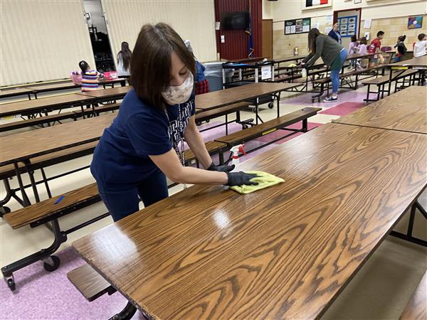 A school employee or volunteer wipes down a lunch table